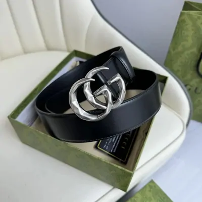 A black Gucci leather belt with a silver double-G buckle, coiled inside its box on a monogram backdrop