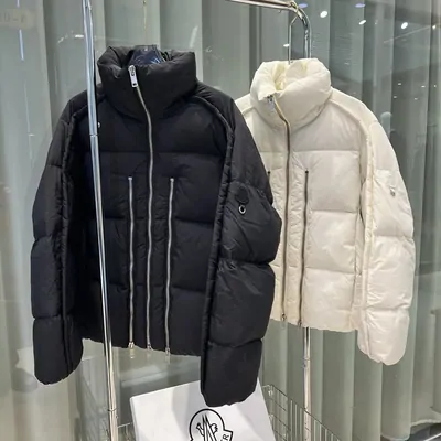 A black puffer jacket and a cream puffer jacket hanging side by side on a chrome rail